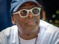 Man wearing a New York Knicks cap and white round glasses, looking to the side outdoors