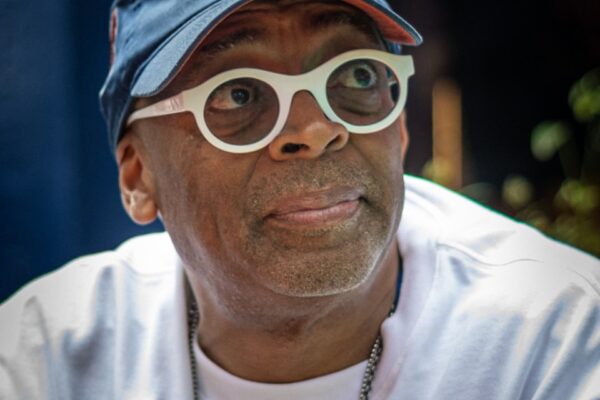 Man wearing a New York Knicks cap and white round glasses, looking to the side outdoors