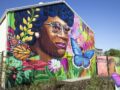 Colorful mural of a woman’s portrait surrounded by flowers and butterflies on a farm house wall