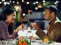 Smile, couple and cheers with wine at restaurant for date, love or holding hands together. Happy man, woman and toast with drink in glass for celebration, anniversary or romance with bokeh at night
