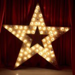 Photo of golden star with light bulbs on red velvet curtain on stage